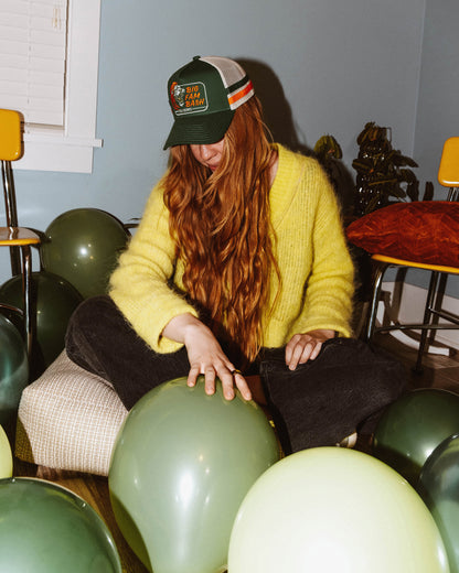 girl wears hat and sits among balloons